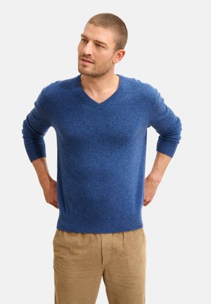 Suéter azul de cuello en V hecho de tejido texturizado, con mangas largas y puños acanalados, combinado con pantalones de pana beige.