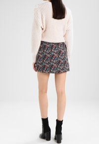 Ljusrosa stickad tröja med avslappnad passform och sänkta axlar, matchad med en mörkblommig minikjol. Modellen bär svarta ankelstövlar.