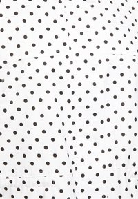 Tissu blanc avec un motif de petits pois noirs uniformément espacés.