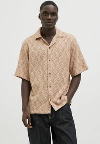 Chemise à manches courtes beige avec un motif en chevrons, dotée d'un devant boutonné et d'un col. Associée à un pantalon en denim foncé.