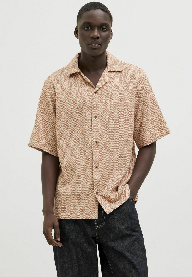 Chemise à manches courtes beige avec un motif en chevrons, dotée d'un devant boutonné et d'un col. Associée à un pantalon en denim foncé.