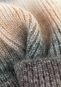 Tessuto di lana lavorato a maglia con sfumature degradate dal beige al grigio, caratterizzato da una texture a coste, fibre morbide e dettagli di cuciture visibili.