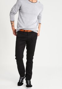 Šedý svetr s dlouhým rukávem a kulatým výstřihem, doplněný černými úzkými kalhotami a černými teniskami s bílou podešví a pruhy. Hnědý pásek jako akcent.