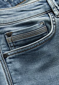 Gaišzilas džinsu bikses ar kontrastējošiem oranžiem diegiem, ar mazu priekšējo kabatu un gludu tekstūru.