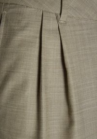 Tissu plissé beige mettant en valeur un tissage fin et texturé. Les détails incluent des coutures subtiles et une finition lisse, soulignant le look sur mesure.