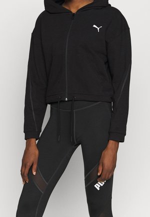 Sweat à capuche noir zippé avec cordons et logo Puma, porté avec un legging noir avec des panneaux en mesh et le texte blanc Puma sur la cuisse.