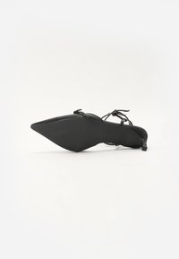 Chaussure noire à bout pointu avec un petit talon, dotée de fines lanières et d'une surface supérieure texturée. Design minimaliste sans embellissements visibles.