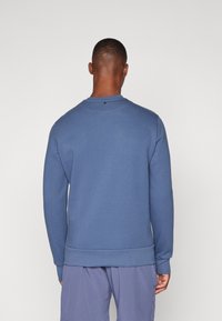 Sweatshirt azul com mangas compridas e decote redondo. Tecido suave, punhos e bainha canelados, com um pequeno detalhe preto nas costas.