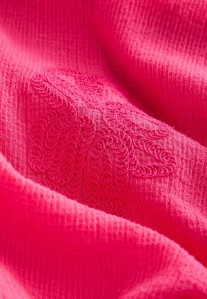 Tissu texturé rose vif avec un motif tissé. Présente des détails brodés de la même couleur, créant un intérêt visuel subtil.
