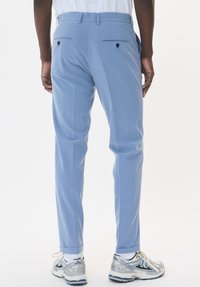 Helleblaue maßgeschneiderte Hosen mit glatter Textur, zwei Gesäßtaschen mit schwarzen Knöpfen und einem leicht umgeschlagenen Saum. Kombiniert mit silbernen Sportschuhen.