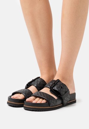Sorte quiltede slidesandaler med en bred strop med spænde, gummisål og åben tå-design, velegnet til afslappet brug.