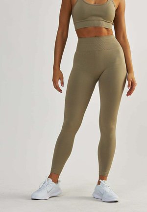 Beige verkürzter Sport-BH und hochtaillierte Leggings aus elastischem Material, kombiniert mit weißen Sportschuhen. Einfaches Design, körpernahe Passform.