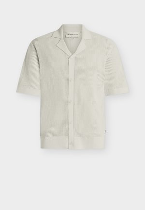 Κοντομάνικο, εκρού πλεκτό πουκάμισο με ανοιχτό γιακά και εμπρός με κουμπιά, που διαθέτει υφή με διάτρητο μοτίβο σε όλο το ύφασμα.