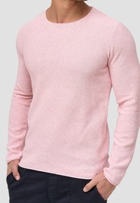 Langärmliger, runder Pullover in sanftem Rosa, mit einem strukturierten Strickmuster und taillierter Passform, kombiniert mit dunklen Hosen.