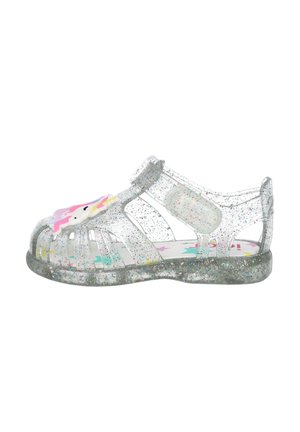 Sandalia infantil transparente con purpurina, con parte delantera cerrada, tira ajustable y una decoración colorida de unicornio en la parte superior.