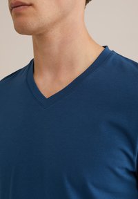 Kék pamut póló V-alakú kivágással. Simaság jellemzi, testhezálló fazon, egyszerű egyszínű, minta vagy díszítés nélkül.