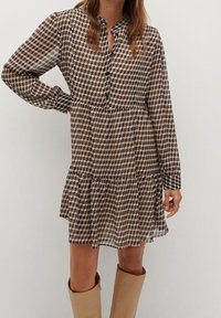 Robe à carreaux marron en tissu léger, dotée d'un devant à boutons, de manches longues, d'une taille froncée et d'une jupe évasée.