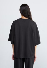 Svart oversized t-skjorte laget av bomull, med rund hals og korte, vide ermer, med en glatt tekstur og avslappet passform.