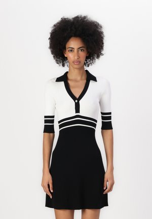 Knit dress featuring a black and white color scheme, short sleeves with stripes, collar, and button detail. Flared silhouette at the skirt.