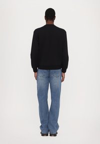 Felpa nera con collo rotondo e orlo a coste abbinata a jeans chiari a gamba larga. Tessuto morbido, taglio comodo e branding discreto.