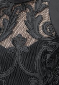 Tessuto in pizzo nero con ricamo floreale intricato su sfondo in rete trasparente.