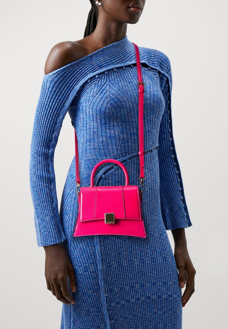 Femme portant une robe bleue côtelée à une épaule avec des boutons et portant un sac à main structuré rose vif avec une poignée supérieure et une bandoulière.