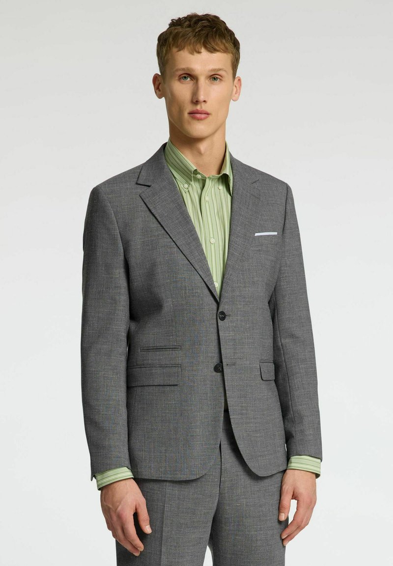 Grijze op maat gemaakte blazer met notch-lapels, twee knopen en zijzakken, gecombineerd met een groen gestreept shirt. Gestructureerde stof, strak design.