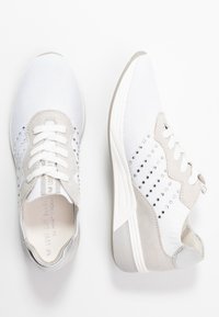 Buty sportowe z białą siateczkową cholewką, srebrnymi akcentami, beżowymi skórzanymi detalami i ozdobnymi cyrkoniami po bokach.