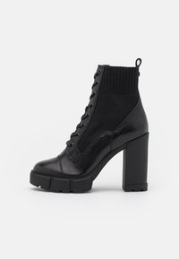 Black heeled ankle boot with a glossy leather front, knitted upper, rounded toe, lace-up design, and thick block heel.