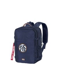 Sac à dos en tissu bleu marine avec une forme carrée arrondie, comportant un logo circulaire blanc, plusieurs zips et une étiquette rouge "TAILLE CABINE D'AVION".