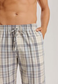 Geklede pyjamabroek met een lichtbeige, blauwe en marineblauwe kleurenschema. Voorzien van een elastische tailleband met een trekkoord en zijzakken.
