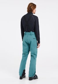 Pantalones de nieve impermeables en tono verde azulado con tirantes negros ajustables y refuerzos en las piernas inferiores. Presenta un logo en la parte trasera y un diseño de corte recto.