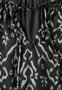 Schwarzer plissierter Stoff mit einem kontrastierenden weißen Ikat-Muster, einem V-Ausschnitt und einer gerafften elastischen Detailierung um den Hals.