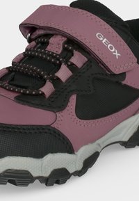 Gros plan sur une basket Geox noire et violette avec une semelle épaisse, des lacets élastiques et une bride Velcro pour un maintien sûr.