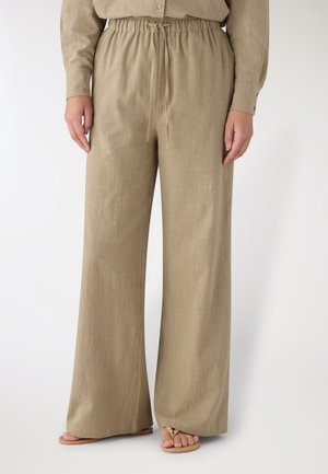 Pantaloni beige a gamba larga in lino con vita elastica e coulisse, indossati con camicia beige abbinata e sandali beige su sfondo bianco.