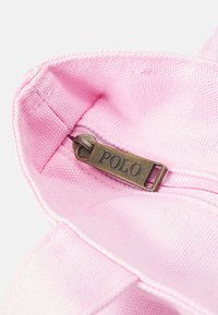 Interior de una bolsa de tela rosa con un zipper de bronce visible etiquetado como "POLO". El forro es suave con una textura sutil.