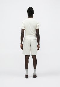 Shorts en coton gris clair à coupe droite, avec des poches arrière détaillées, associés à une chemise crème ajustée et des chaussettes grises. Design simple et épuré.