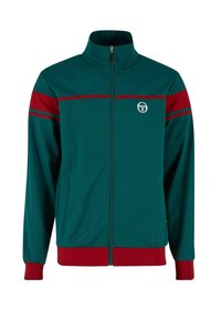 Jachetă verde cu fermoar și guler înalt, cu dungi roșii pe umeri și la tiv, și un logo circular pe piept.