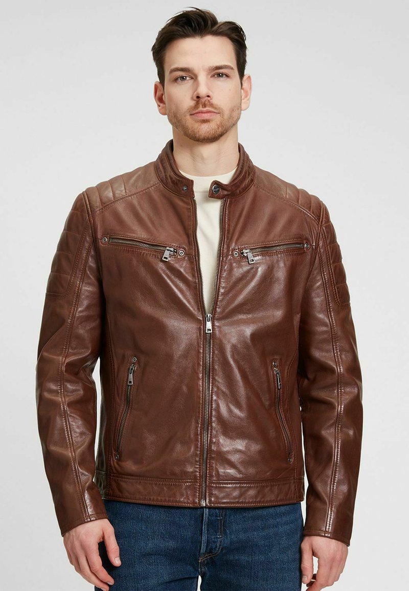 Chaqueta de moto de cuero marrón con cuello alto, acentos acolchados en los hombros y cremalleras plateadas en el pecho y los bolsillos laterales.