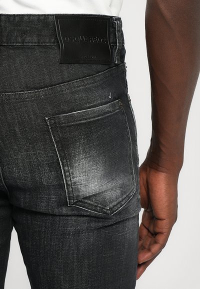 Jeans de mezclilla gris oscuro con un acabado texturizado, que presentan un gran bolsillo trasero y una etiqueta de parche de cuero negro en la cintura.