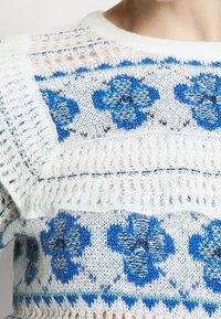 Sweter dzianinowy w białym i niebieskim kolorze z kwiatowymi wzorami. Posiada teksturowany wzór oraz otwarte sekcje dzianiny wzdłuż dekoltu i rękawów.