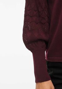 Burgundy pullover med texturerade stickade ärmar som har ett diamantmönster. Fitted muddarna och det släta kroppsmaterialet framhäver dess design.