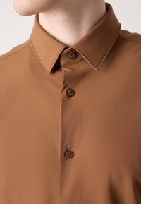 Camicia marrone, con bottoni e colletto classico. Realizzata in un tessuto liscio e texturizzato, con bottoni coordinati e una leggera lucentezza.