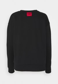 Sudadera negra con un corte holgado, puños acanalados y cuello redondo. Presenta una etiqueta roja con la palabra "HUGO" en la parte trasera. Textura de tela suave.