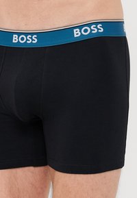 Boxeri negri din bumbac, cu talie albastră pe care este inscripționat "BOSS" în alb. Material elastic din bumbac, croială strânsă, cu cusături plate și fără modele.