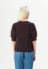 Burgundy short-sleeve knit sweater with a round neckline, featuring puff sleeves and ribbed hem, paired with light blue high-waisted jeans.