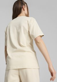 Camiseta de algodón beige con un ajuste relajado, mangas cortas y un dobladillo recto, con detalles de costura sutiles y una etiqueta en el lateral.