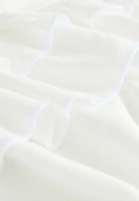Un tissu blanc avec une texture douce et lisse présente des volants froncés avec un subtil éclat et de fines coutures blanches le long des bords.