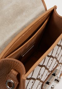 Brązowe skórzane wnętrze torebki o teksturowanym wykończeniu. Wnętrze wyposażone jest w paskowane podszewkę i metaliczne zapięcie.