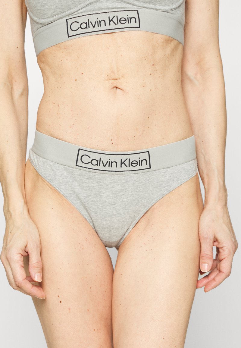 Shorts en coton gris avec une large ceinture élastique portant le logo "Calvin Klein" en noir. Coupe mi-haute et texture lisse.